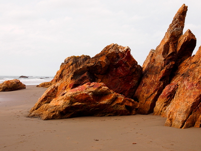 [Orange gold red rock with fractured edges sits on the sand.]